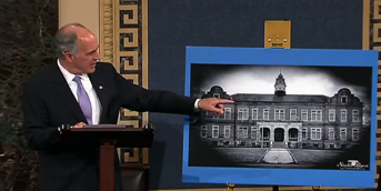 Senator Bob Casey on the Senate floor pointing at a photo of an institution