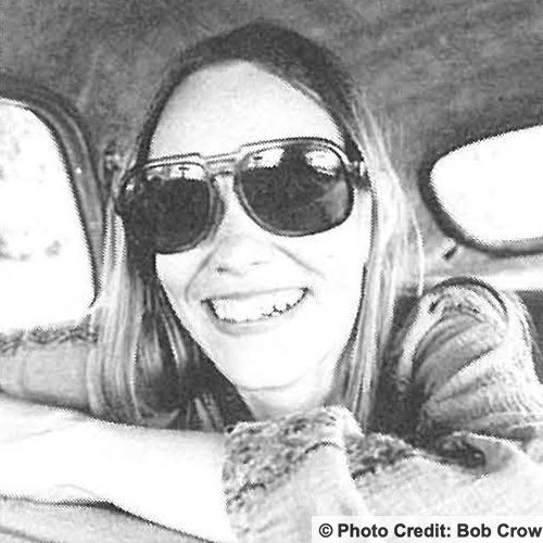 Woman in back seat of car leaning on front seat smelling wearing sunglasses. Photo credit to Bob Crow