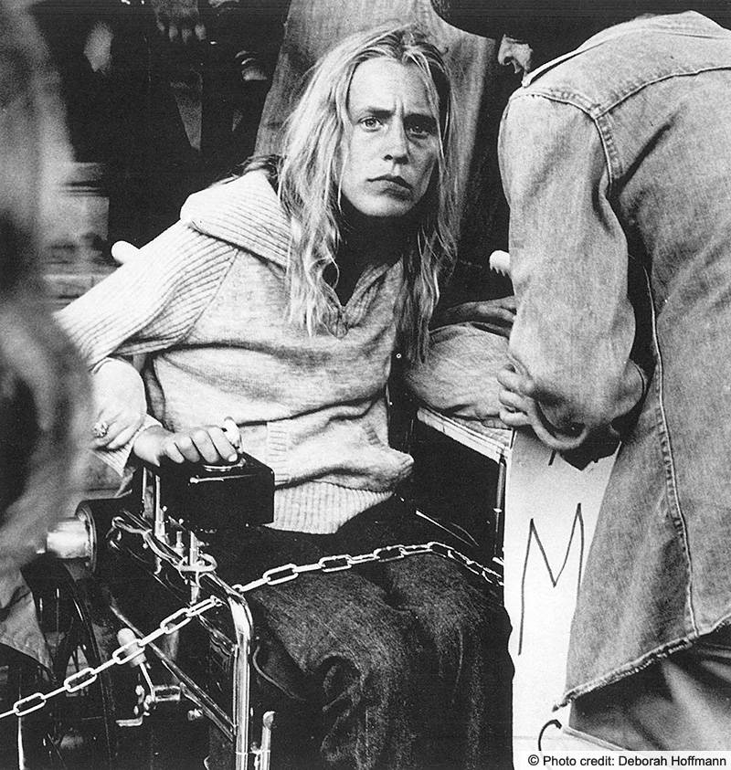 A woman using her wheelchair at a demonstration. The wheelchair is chained to something that we can't see. Photo credit: Deborah Hoffmann