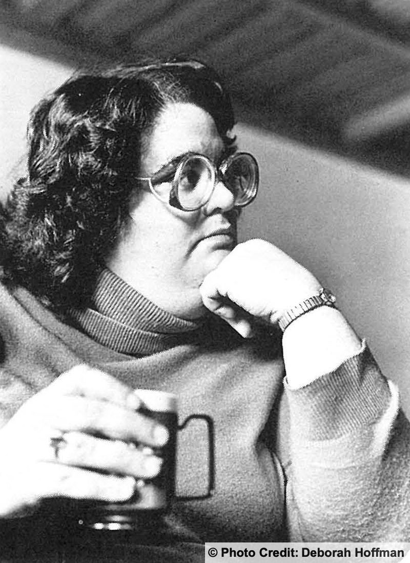 Woman seated at a table. Coffee cup in one hand and her chin rests on her other hand. Photo credit: Deborah Hoffman