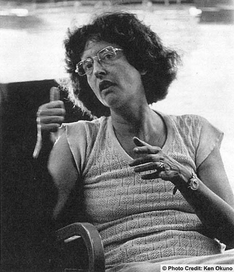 A woman seated and gesturing with her hands as she speaks. Photo Credit: Ken Okuno