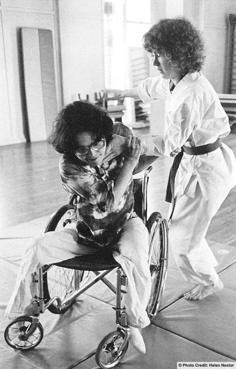 A self defense class. The student is a wheelchair user and the instructor has her in a neck hold. Photo credit: Helen Nestor