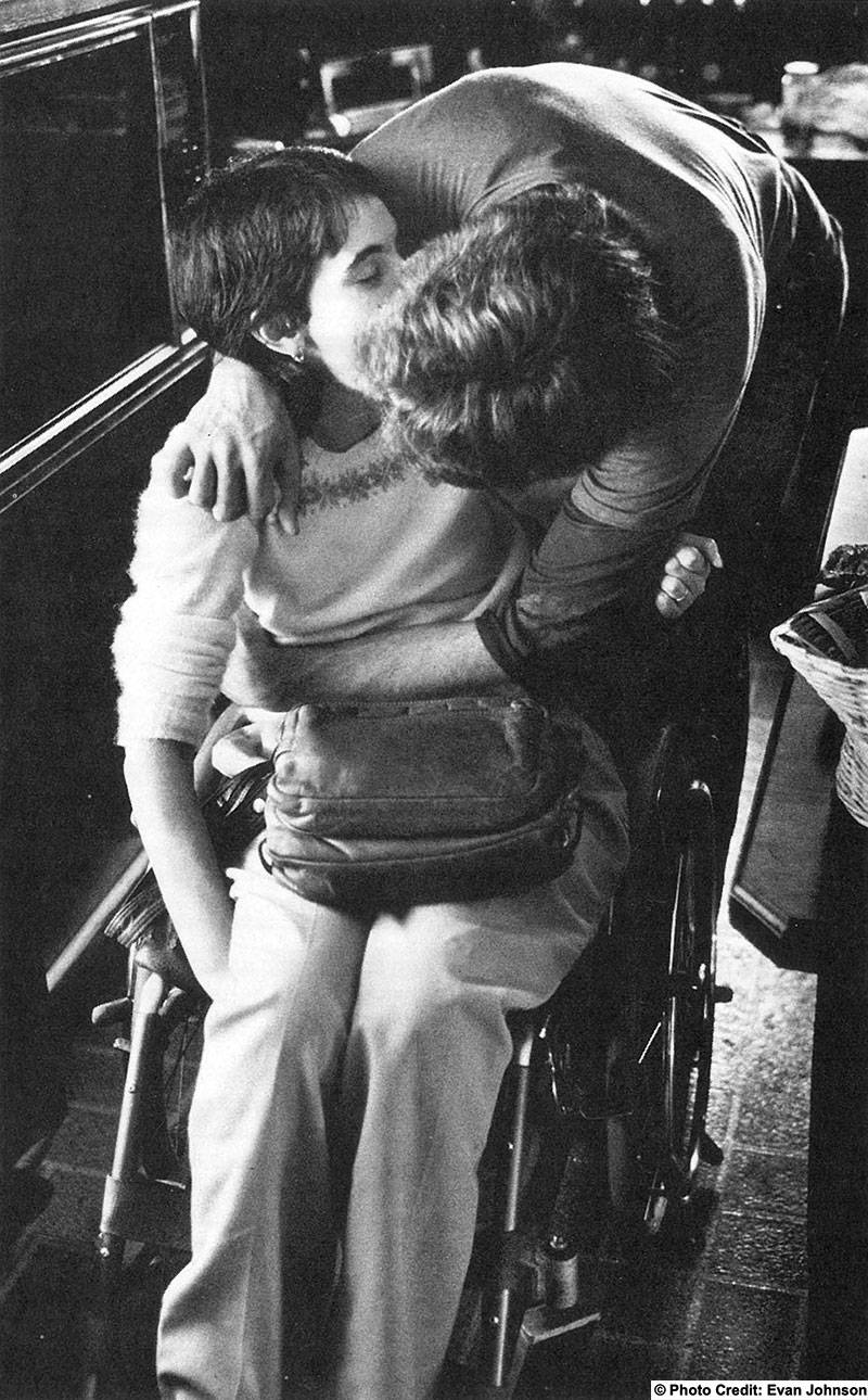 A man is leaning over to kiss a woman in a wheelchair. Photo Credit: Evan Johnson