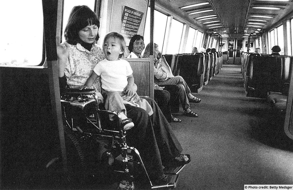 A wheelchair user riding public transit with a young child on her lap. Photo credit: Betty Medsger