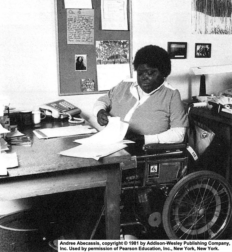 A woman sits in her wheelchair working at her desk. Photo credit: Andree Abecassis