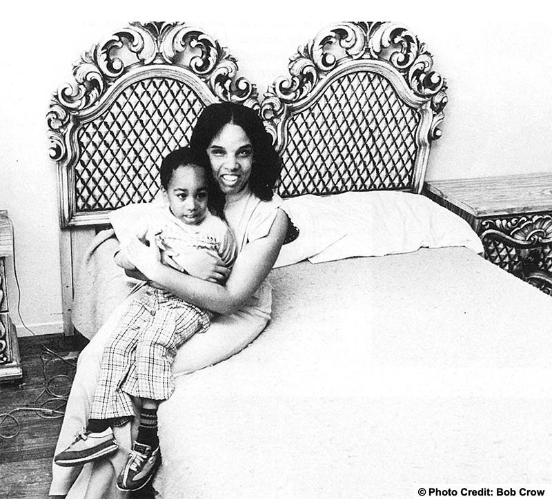 Woman sitting on the edge of her bed holding her 6 to 8 year old son on her lap.