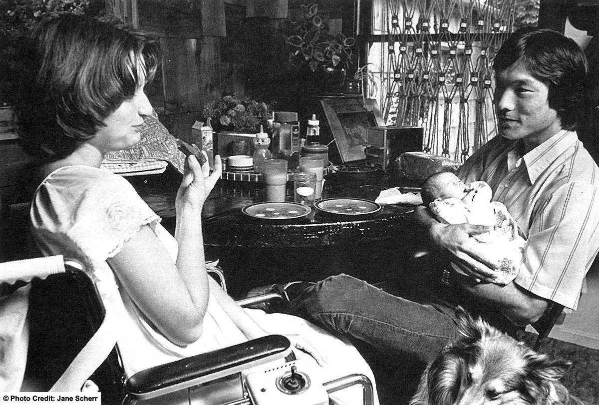 Mother and father are at the breakfast table. The father is holding the infant and the mother is seated in her wheelchair. Photo credit: Jane Sherr