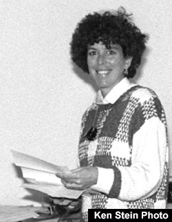 Arlene Mayerson standing with papers in hand smiling and looking at the camera. Ken Stein Photo