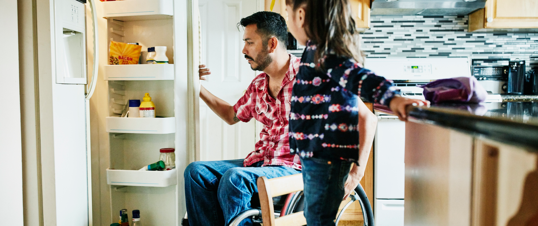 A wheelchair users opens the refrigerator next to their child
