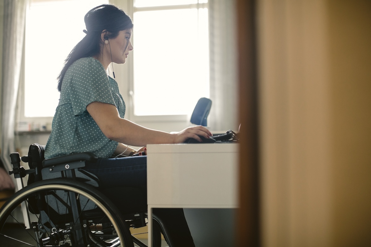 Side view of young disabled freelance worker using computer at desk in room