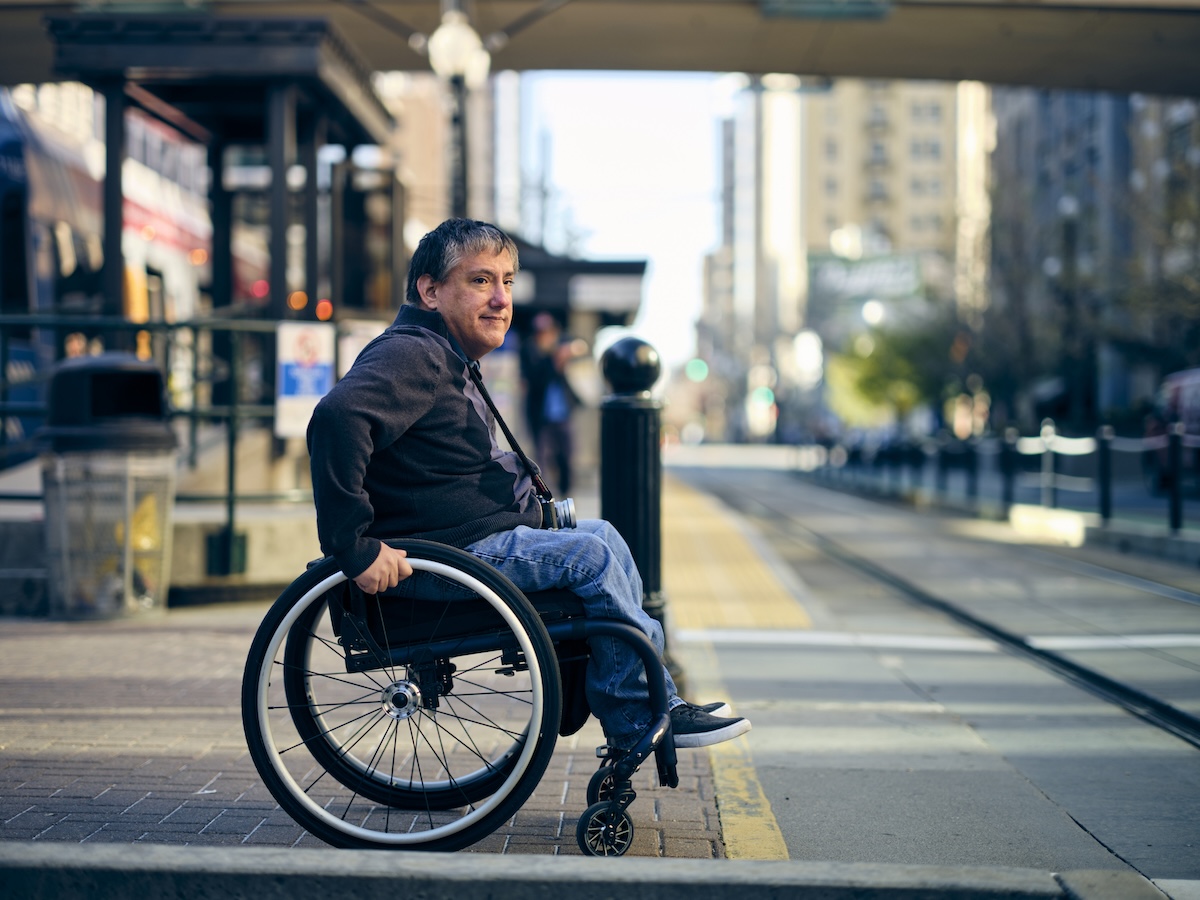 A person presenting as male and white uses a wheelchair and waits for the bus