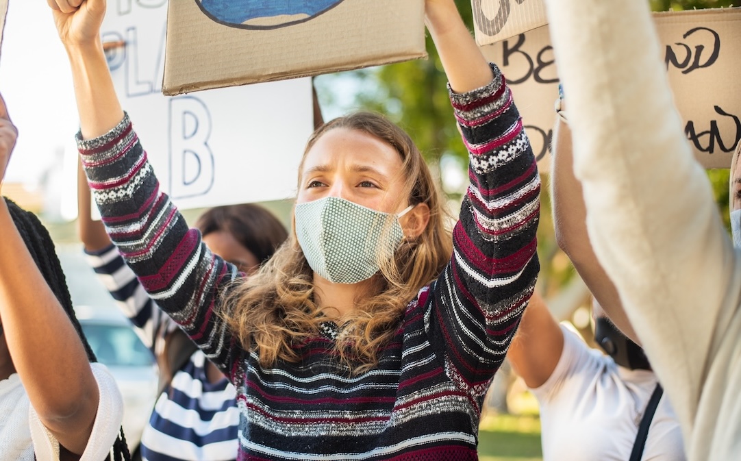 Young female presenting white person holding up a cardboard sign during a protest.