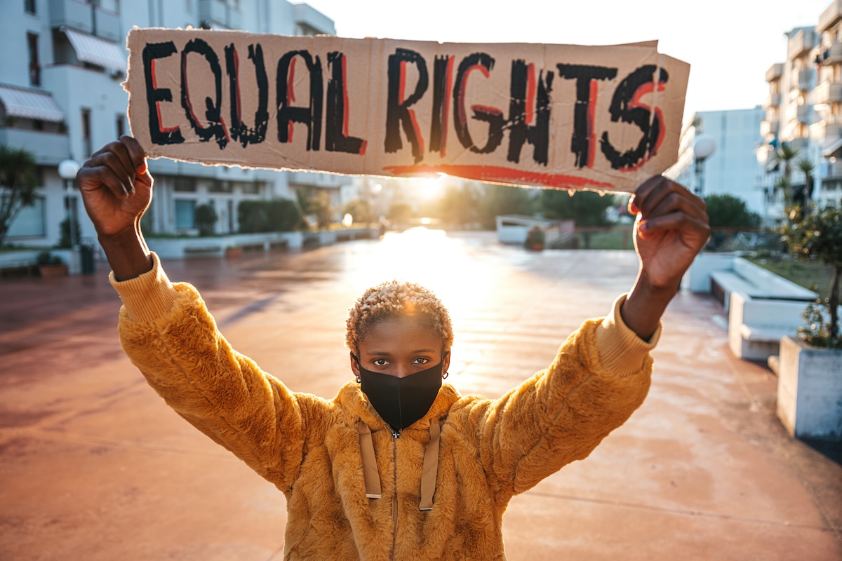 A young black female presenting person holds up a sign that reads equal rights.