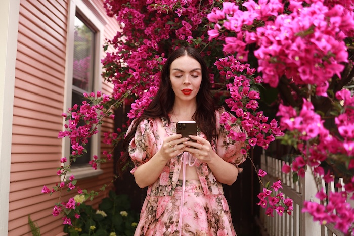 A female presenting person with autism on their cell phone outside a big flowery plant