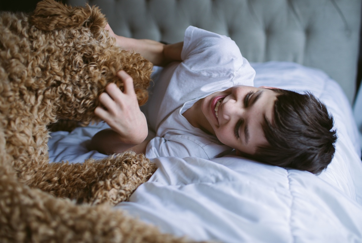 Young boy with autism playing in bed with golden doodle service dog