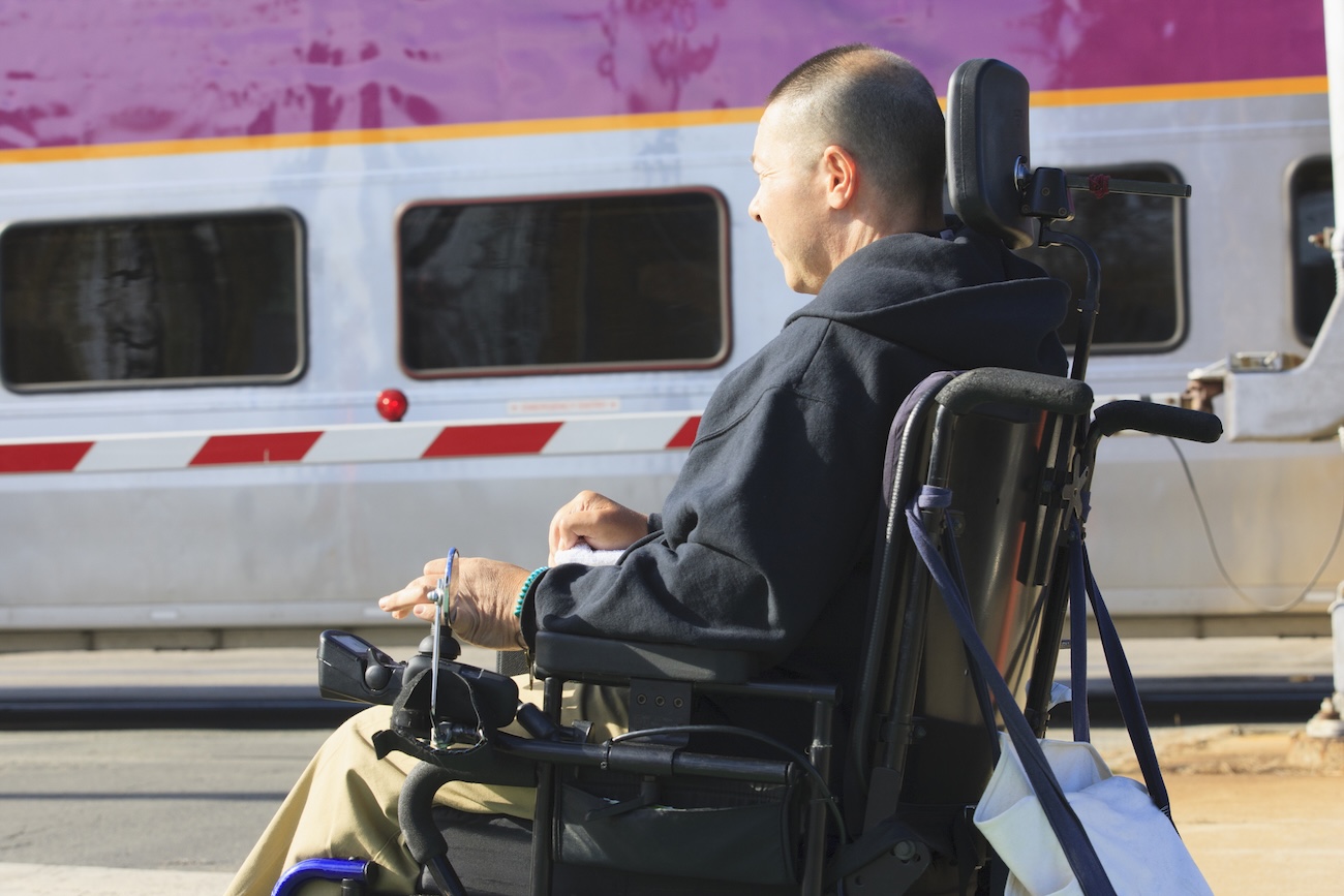 Person using a power wheelchair in front of the side of an Amtak train