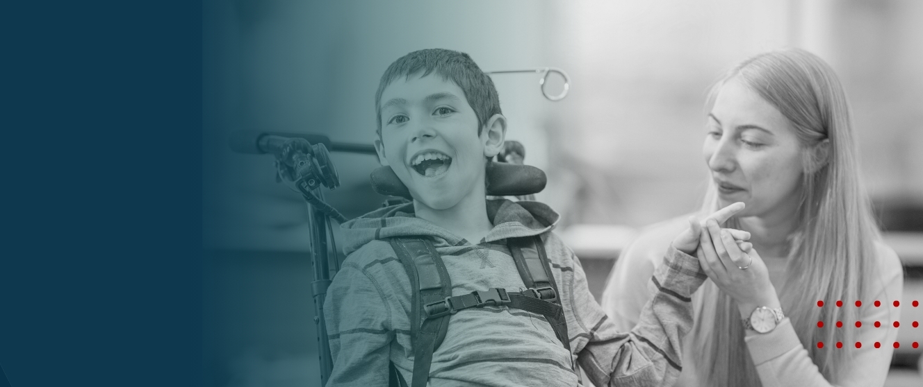 A young feminine presenting person crouches next to a masculine presenting child in a wheelchair