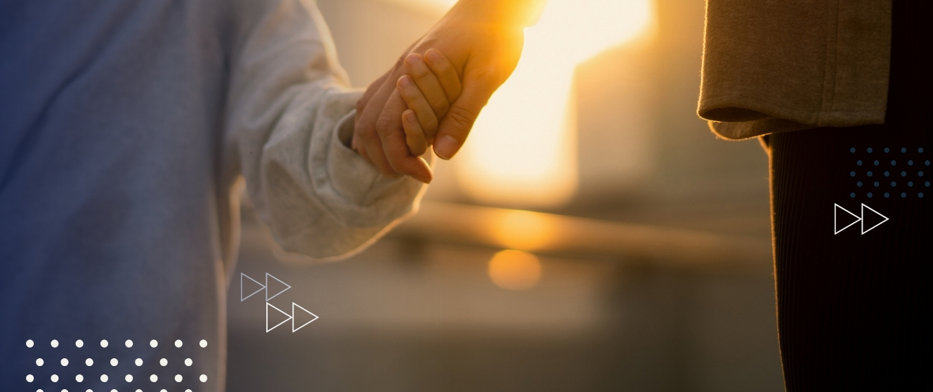 A younger person and a parent figure hold hands in a sunset