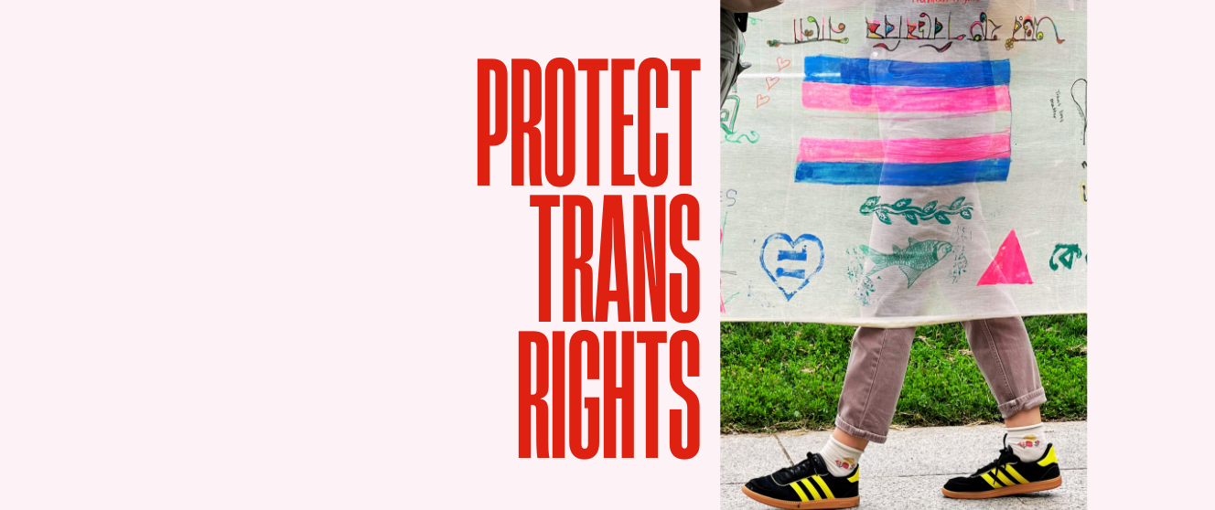 A person walking in Adidas shoes holds a banner with hand-drawn images, one of which is a trans pride flag. Text reads 