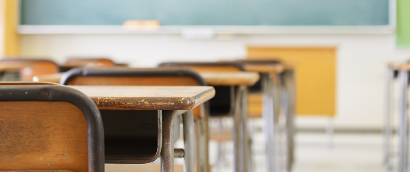 An empty classroom with rows of desks and a chalkboard.